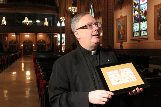 <p>Rev. Boland holds up the certificate from the Vatican that declares the authenticity of Holy Family's recently acquired relics.The church received the relics as a gift for its 155th anniversary.</p>
