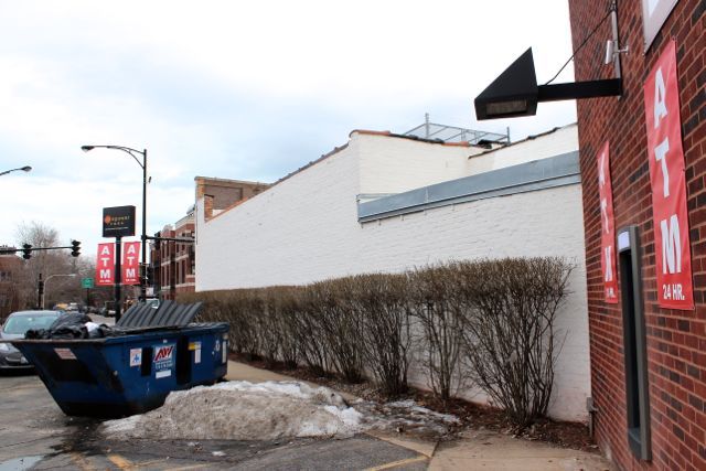 <p>A 24-Hour ATM was installed at 1704 N. Milwaukee Ave. on the southern end of a strip mall, in front of a handicap parking space, obscured by a garbage bin and next to a wall and bush. A security camera is positioned above the machine along with bright lights.</p>
