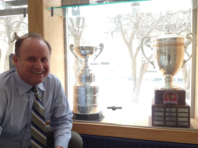 <p>St. Rita hockey coach Craig Ferguson poses in front of the team's 2012 and 2010 state championship trophies at the school.</p>
