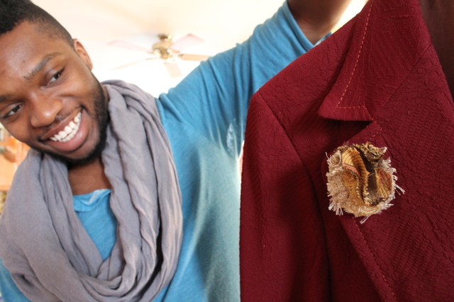 <p>Pilsen designer Redgi Woods holds up a men's jacket with a lapel pin he designed. After recently attending New York's fashion week, Woods said men's fashion &mdash; and accessories &mdash; are currently hot.</p>
