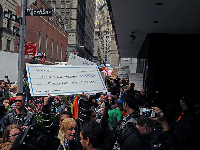 Protesters carried a mock check for Jamie Dimon showing how much he is projected to get back this year after the millionaires tax is allowed to expire in December. 