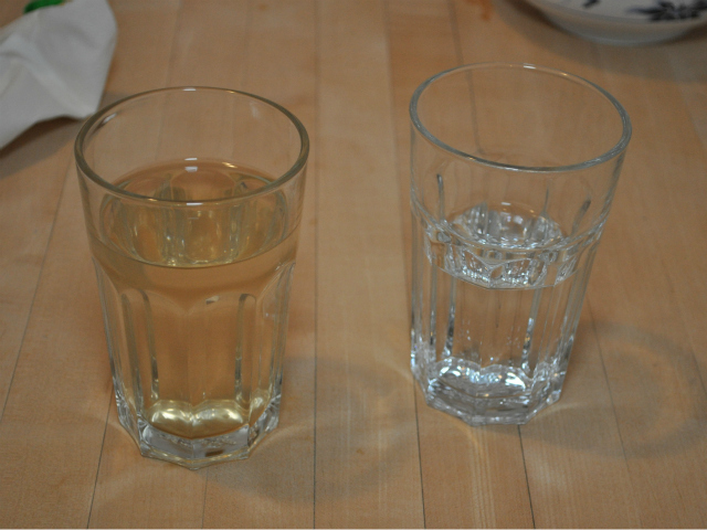 A side-by-side comparison of water samples from the Keithley home. To the left, a glass of brown water from the faucet. To the right, a glass of distilled water.