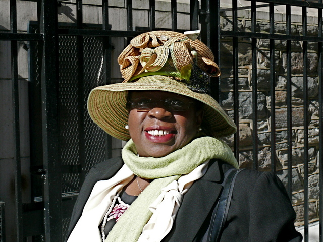 Mattie S. wears a medium brimmed straw hat with ribbon like motif and grassy green accents.