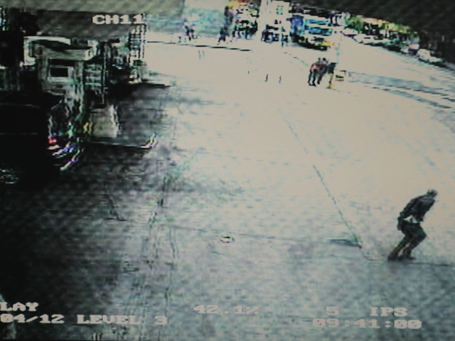 A still from the surveillance video at the gas station shows a man in the lower right corner — a retired lieutenant — reaching for his gun as the robbery suspect runs from the scene. 