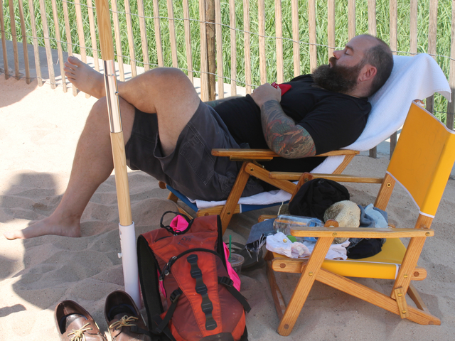 Adults rest under umbrellas in the beach area. 