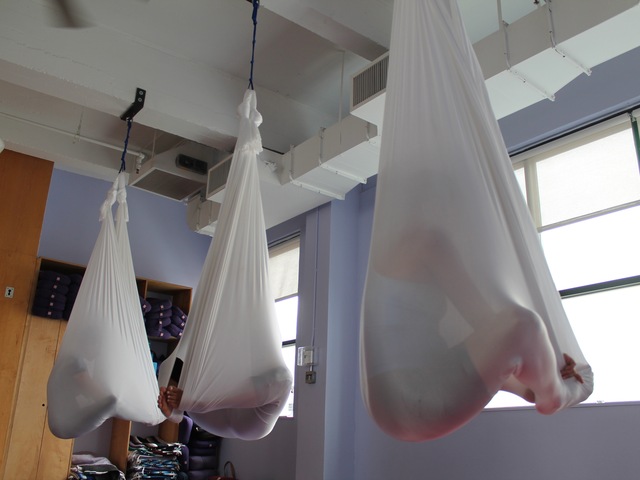 Aerial yoga features students contorting their bodies in fabric hammocks.