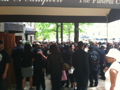 Attendees of the funeral spill out onto the sidewalk.