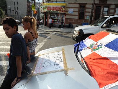 Friends sit on a car with a memorial to Reynaldo Cuevas, who was shot accidentally by a cop while fleeing an armed robbery at his bodega.