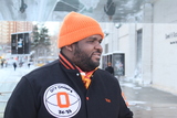 <p>Reuben "Big Rube" Harley wears an orange beanie with a scarf and jacket with orange accents.</p>
