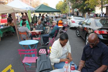  While participants in a temporary farmer's market at a traffic triangle on 150th Street and Macombs Place handed out samples of free food and fresh apple cider Thursday afternoon, residents from the Dunbar Tenant's Association sat on the sidewalk in protest. They say plans to close of a portion of Macombs Place at 150th Street to create a pedestrian plaza with a five-days-per week farmer's market will prevent seniors and the disabled from using the curb for pickup and that the plan is being imposed on them. 
