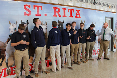  The students responsible for "The Natir" gather in the hallway of St. Rita High School under the watchful eye of English teacher Tim Baffoe (right). The satirical online publication has survived despite the loss of the school's traditional newspaper "The Ritan." 