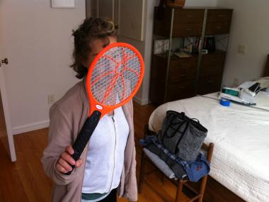 Pauline Galiana holds up an electronic mosquito swatter, one of her first lines of defense against the cloud of mosquitoes that infest her neighborhood.