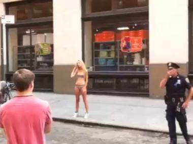 A blond model poses for pictures on a SoHo street while an NYPD officer looks on.